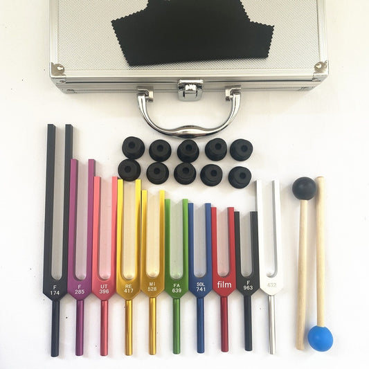 Set of ten colored Solfeggio therapeutic tuning forks with rubber mallets and a premium aluminum case, top-down view on a white background.